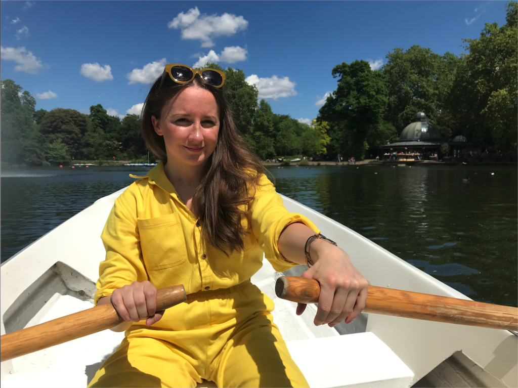 NCMH Research Champion Elin who has brown hair and is wearing a yellow jumpsuit while rowing a boat and smiling at the camera