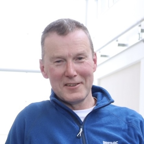 A photograph of Dave, NCMH Champion. He is a white, middle aged man with close cropped hair and is smiling at the camera wearing a blue jumper.