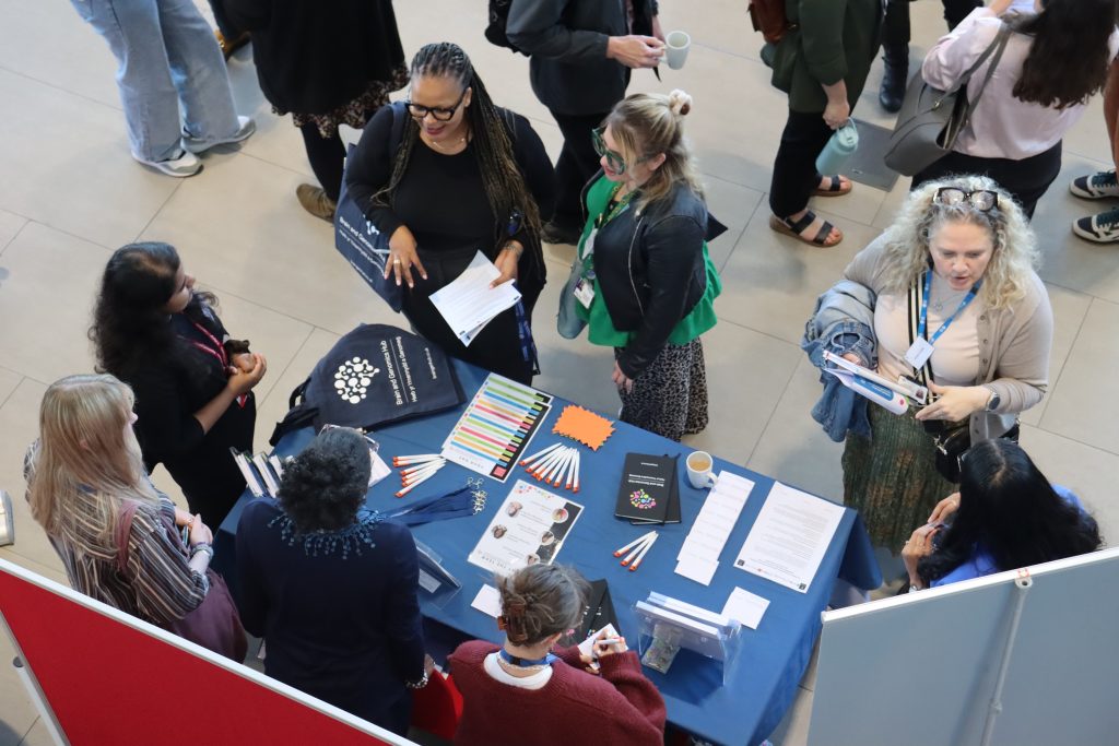 An overhead shot of a busy table at a conference, where visitors are speaking to researchers about taking part in research.