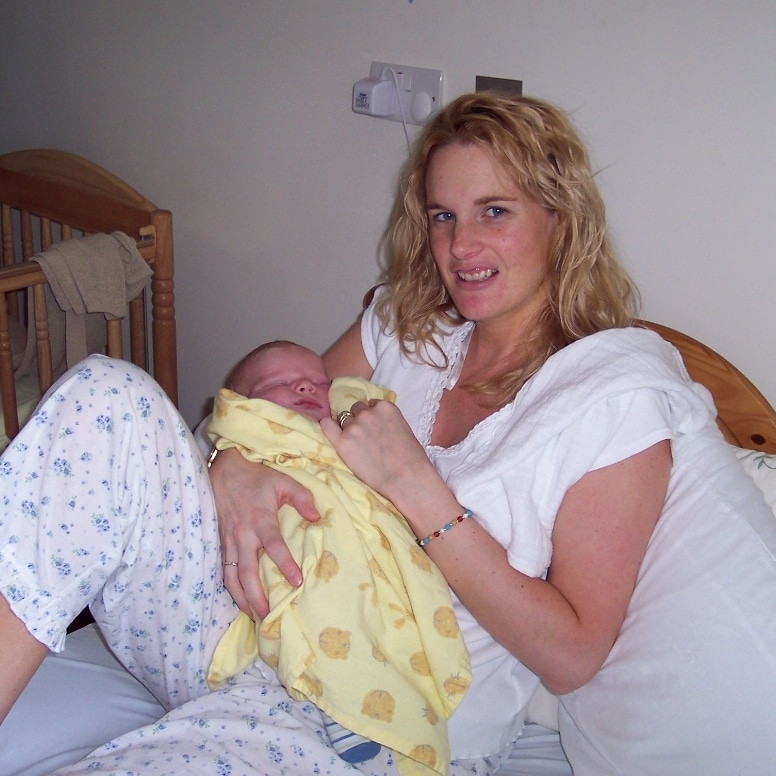 A picture of Barbara, a white blonde-haired woman lying in bed holding a newborn baby.