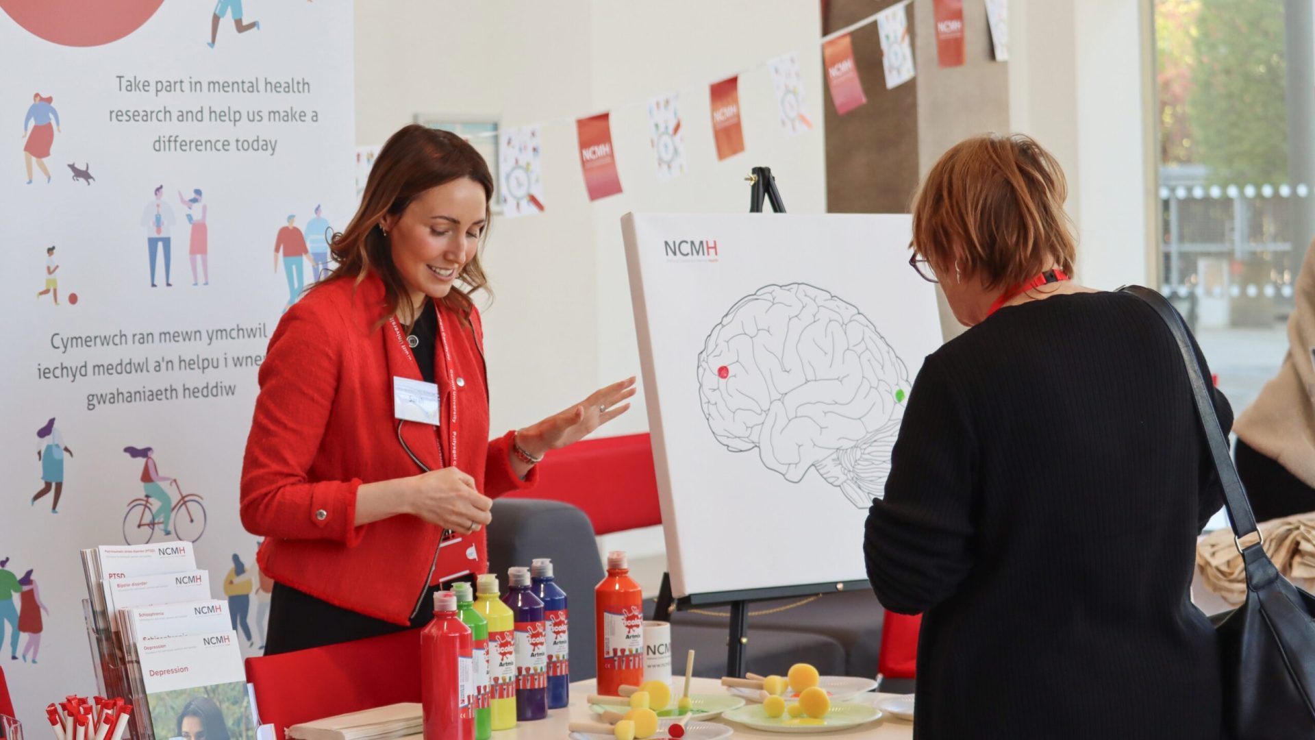 A photo of NCMH Centre Manager Dr Sarah Knott at the NCMH stand talking to an attendee