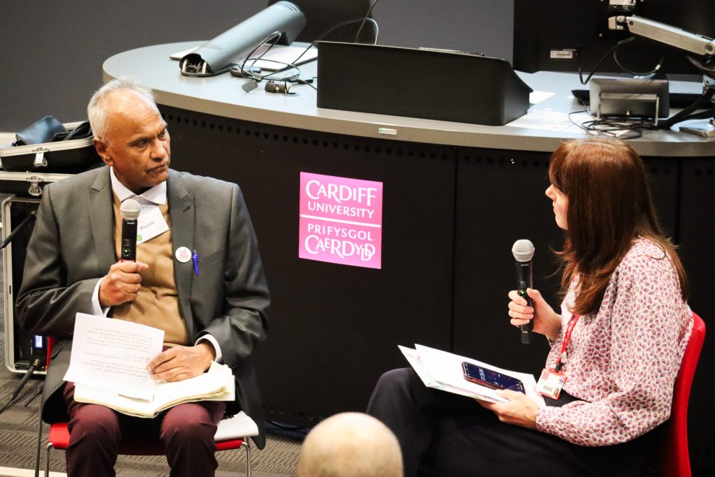 A photo of Dr Sarah Rees (right) interviewing Mustak (left) sitting opposite each other in a lecture theatre holding microphones