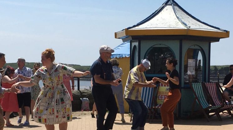 A wide angle photo of Catrin dancing on a sunny pavilion with lots of other couples