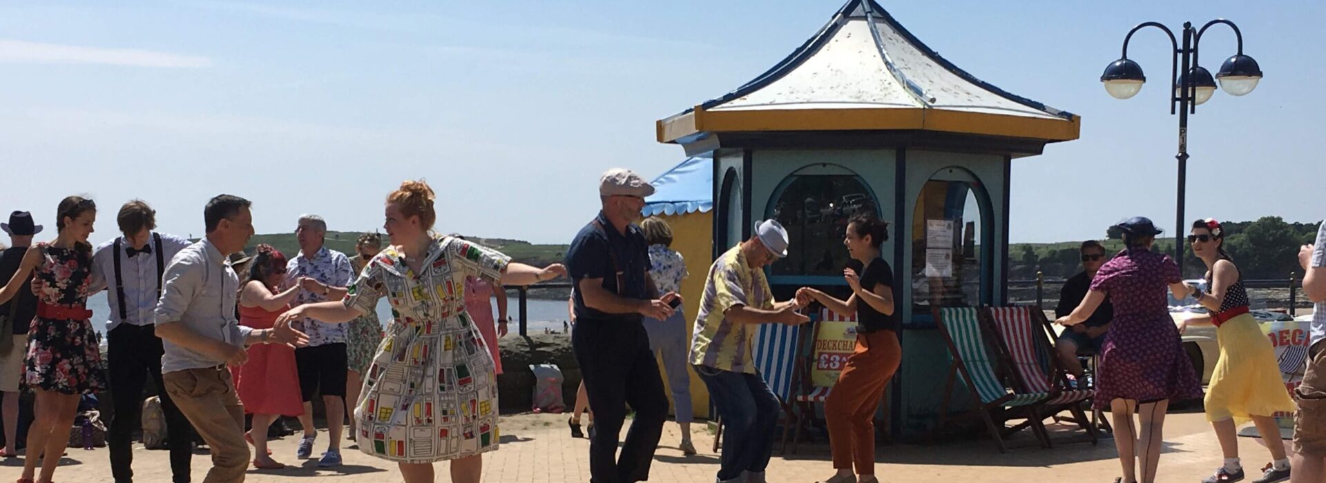 A wide angle photo of Catrin dancing on a sunny pavilion with lots of other couples