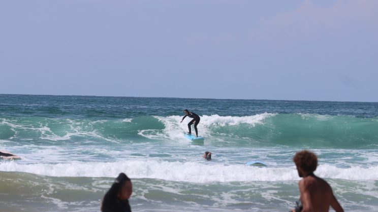 A wide-angle picture of Chloe surfing on a sunny beach in Portugal