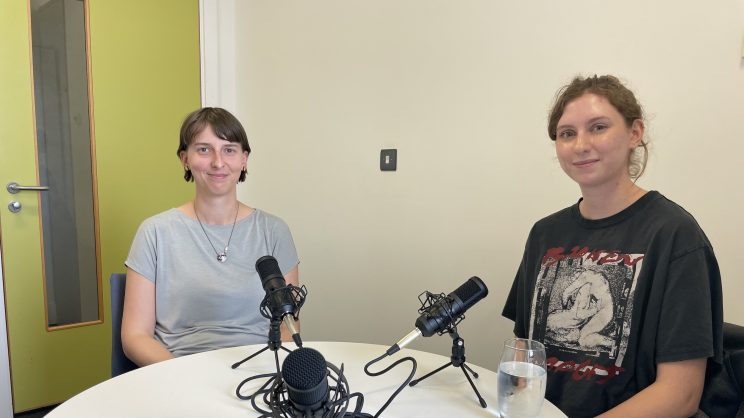 A photo of Dr Joanna Martin (right) and Ellie (left) sitting at a table infront of podcast recording equipment