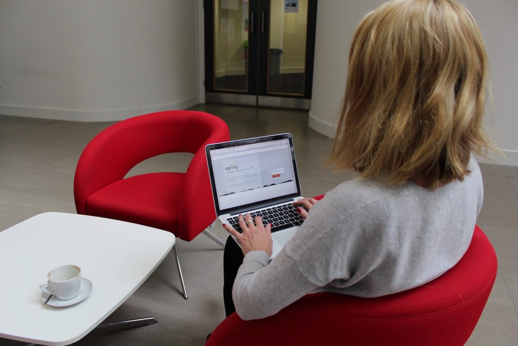 A blonde white woman sat down with her back to the camera using a laptop that reads Spring