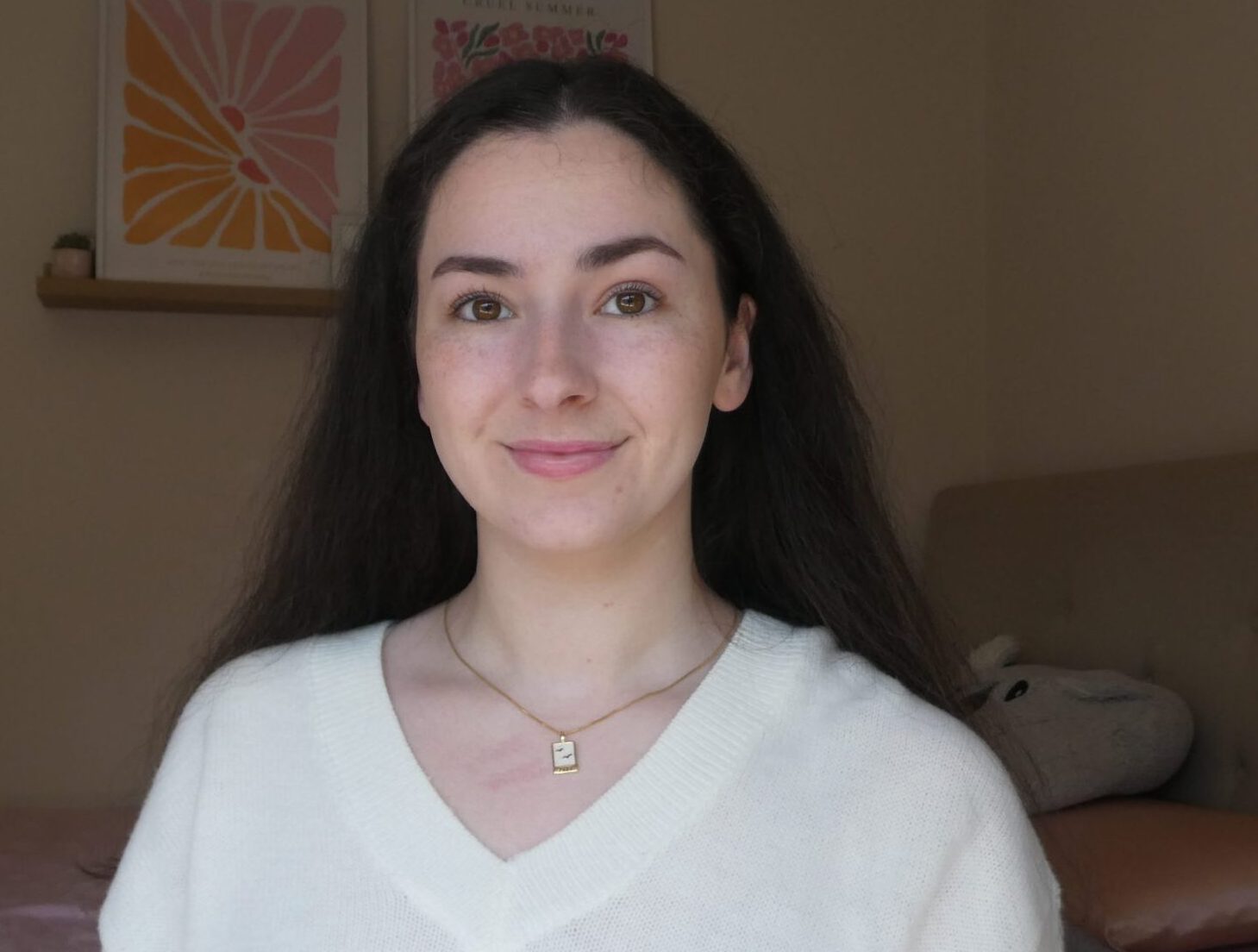 Saskia is a young white woman with long brown hair and she is wearing a white jumper and smiling at the camera.